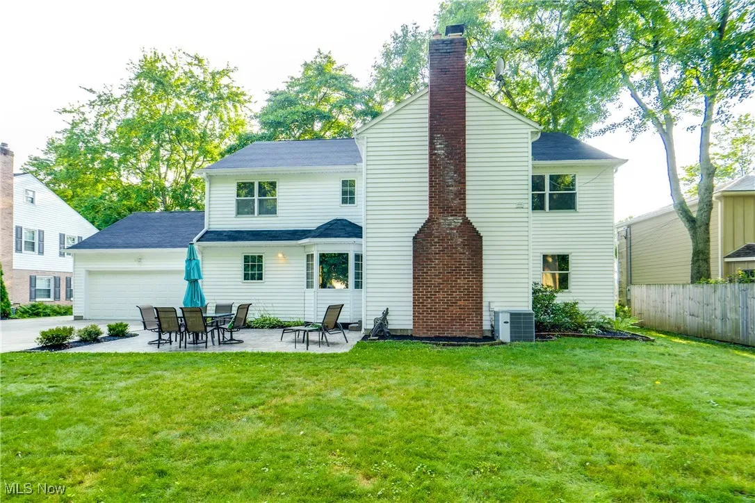 Back of property featuring a chimney, a garage, driveway, and a patio