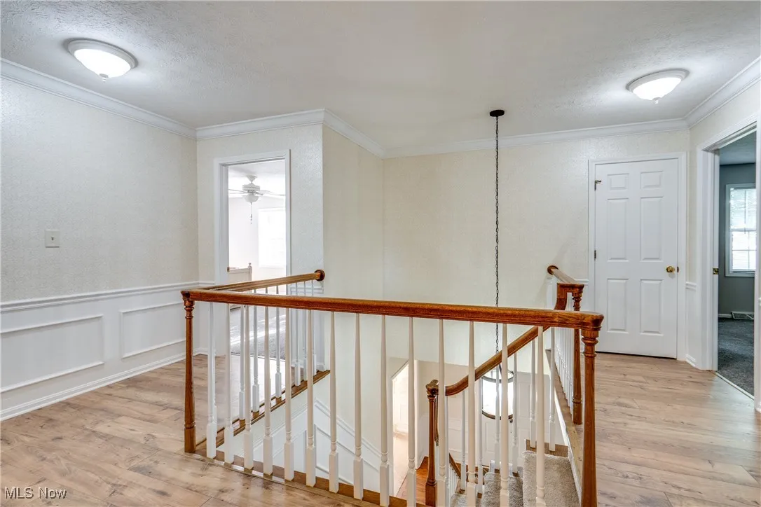 Hallway with an upstairs landing, light wood-style flooring, ornamental molding, a decorative wall, and a textured ceiling