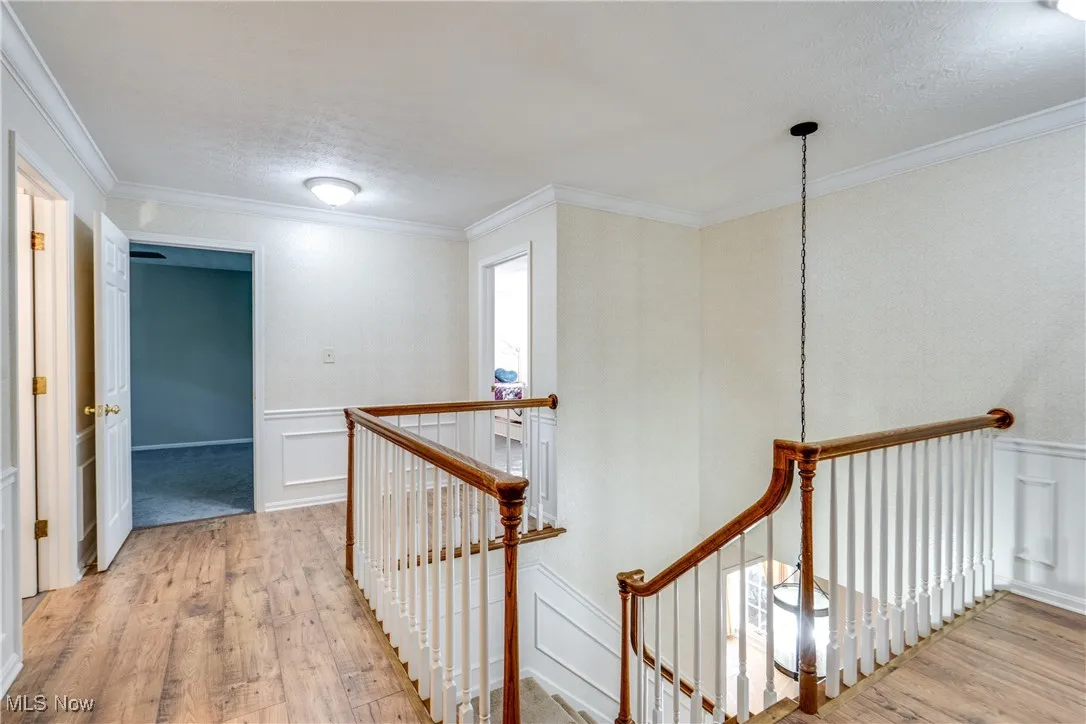 Hall with an upstairs landing, hardwood / wood-style flooring, a decorative wall, wainscoting, and crown molding