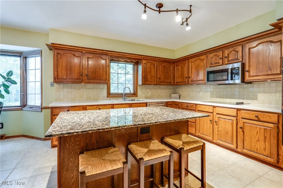 Kitchen featuring a kitchen breakfast bar, stainless steel microwave, a kitchen island, and decorative backsplash