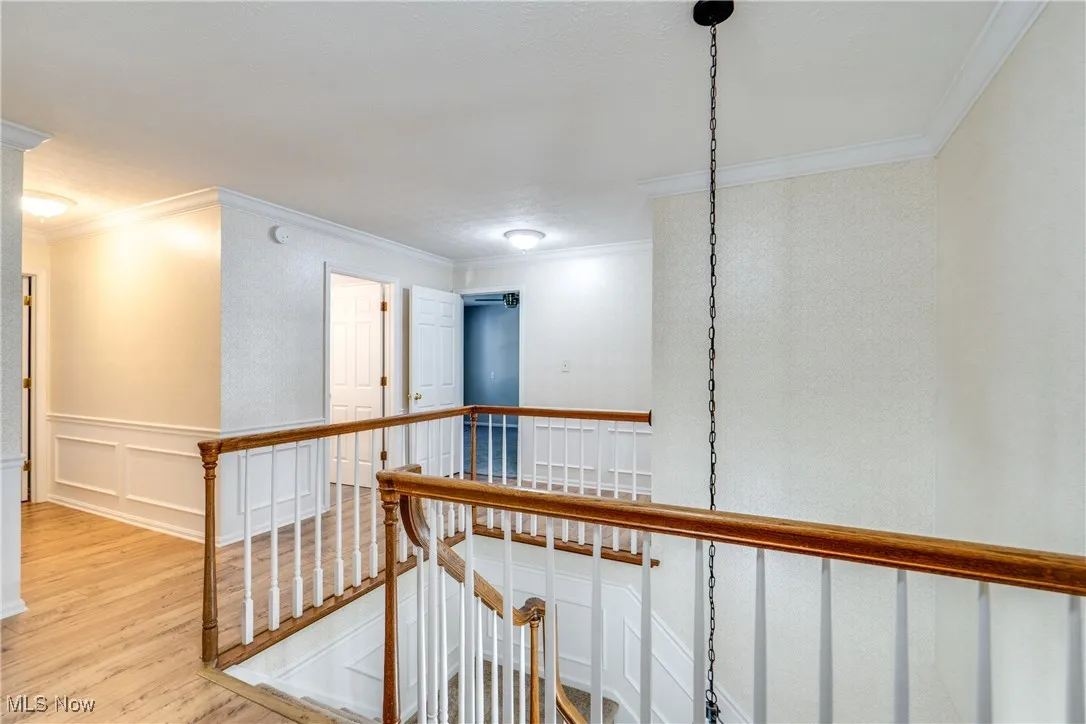 Hall featuring an upstairs landing, light wood finished floors, crown molding, a decorative wall, and wainscoting