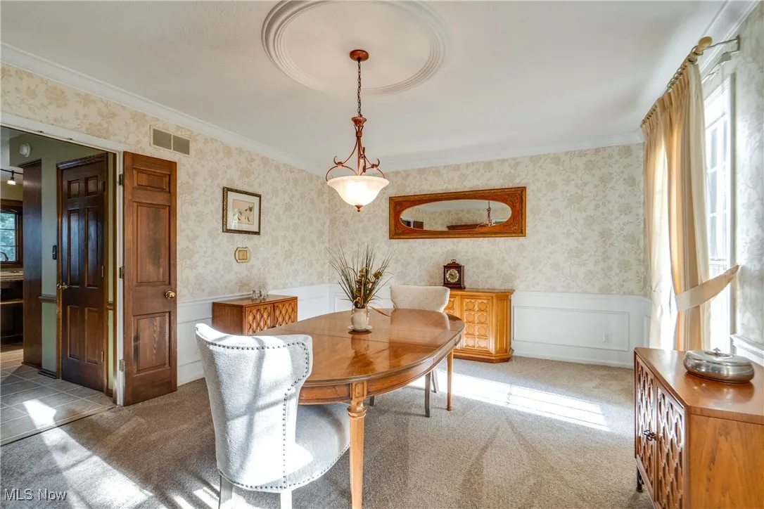 Carpeted dining room featuring wainscoting, ornamental molding, and wallpapered walls