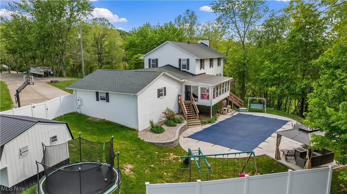 Back of house with stairs, a trampoline, a sunroom, a fenced backyard, and a gate