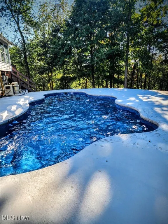 Swimming pool featuring stairs, a patio, and view of wooded area