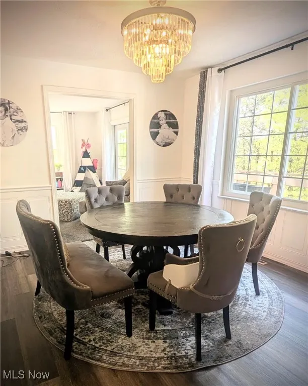 Dining room with a decorative wall, a chandelier, plenty of natural light, dark wood finished floors, and a wainscoted wall