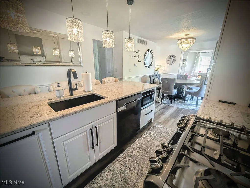 Kitchen with a chandelier, cooktop, wood finished floors, and black dishwasher