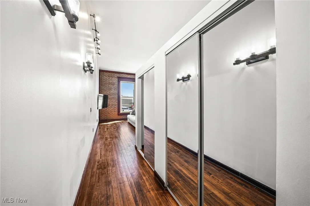 Hallway with brick wall, dark wood finished floors, and rail lighting