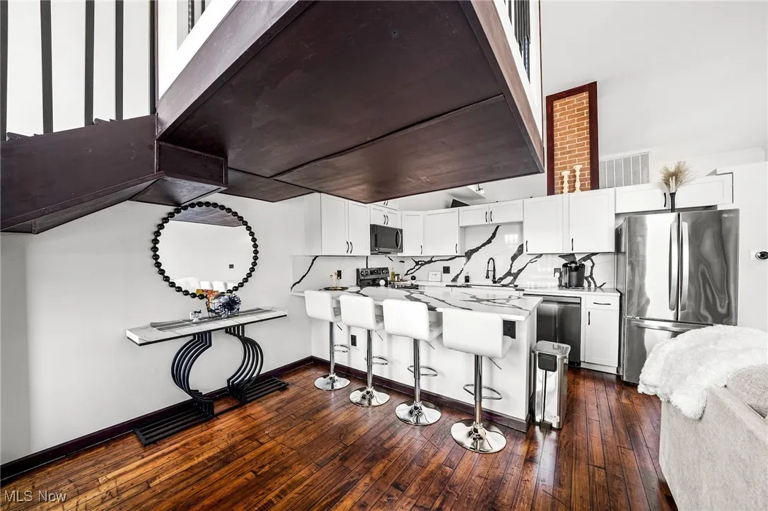 Kitchen featuring appliances with stainless steel finishes, a peninsula, a kitchen breakfast bar, white cabinets, and dark wood-style floors