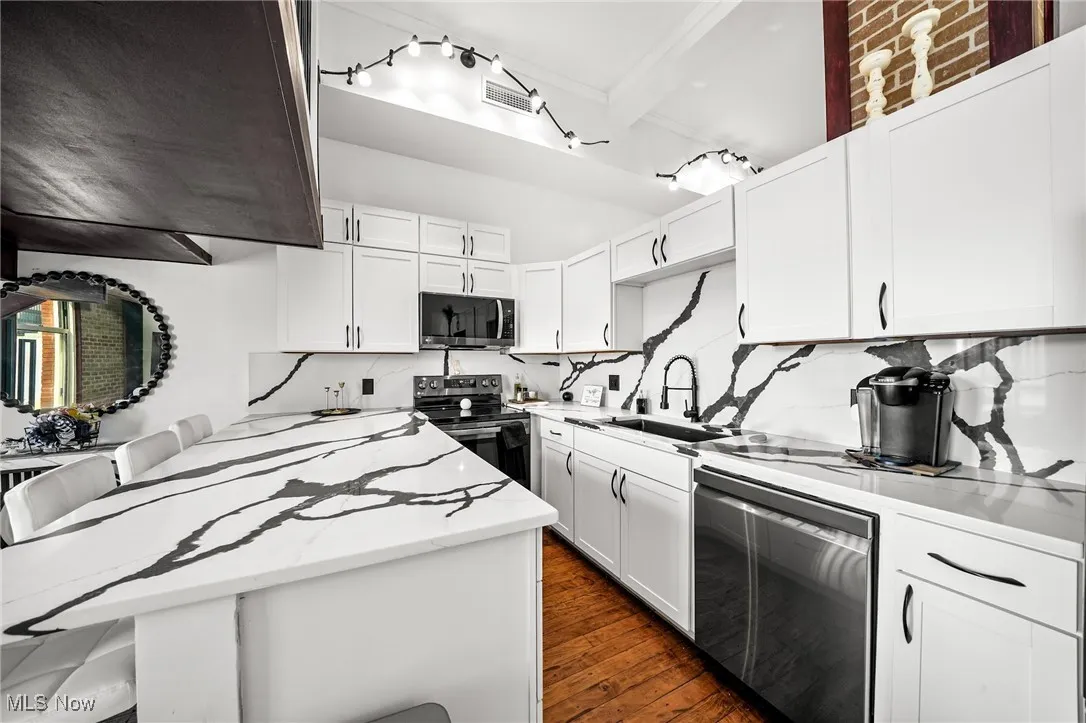 Kitchen with stainless steel appliances, light stone counters, tasteful backsplash, dark wood-style floors, and white cabinets