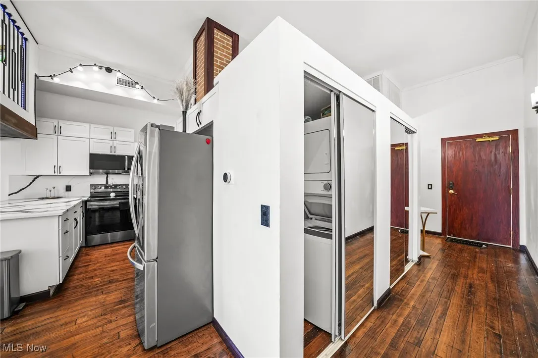 Kitchen with stacked washer / dryer, stainless steel appliances, light countertops, white cabinetry, and dark wood-style flooring