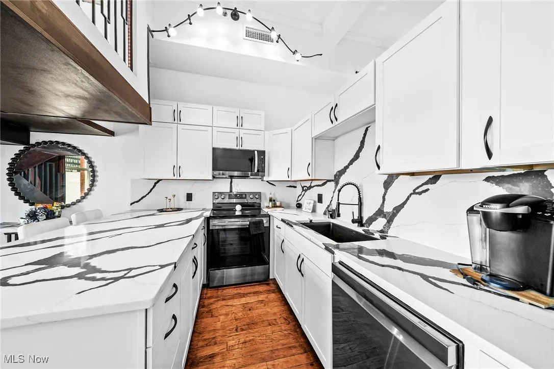 Kitchen with stainless steel appliances, light stone counters, dark wood finished floors, and white cabinets