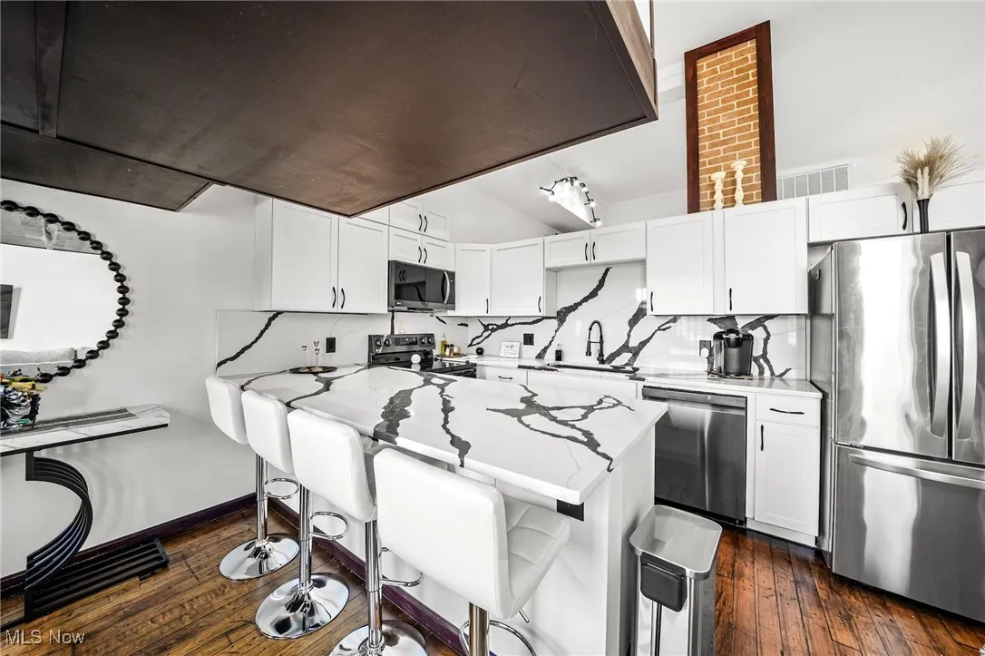 Kitchen featuring stainless steel appliances, white cabinets, a breakfast bar area, and dark wood finished floors
