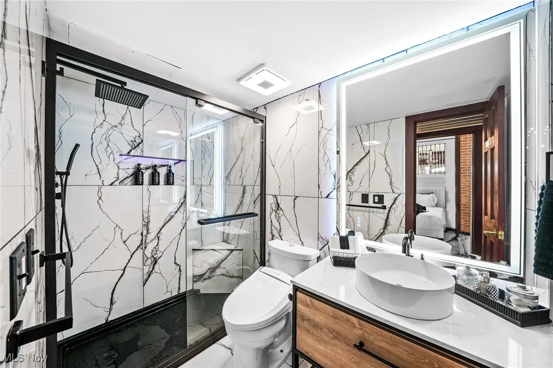 Bathroom with vanity, a marble finish shower, and tile walls