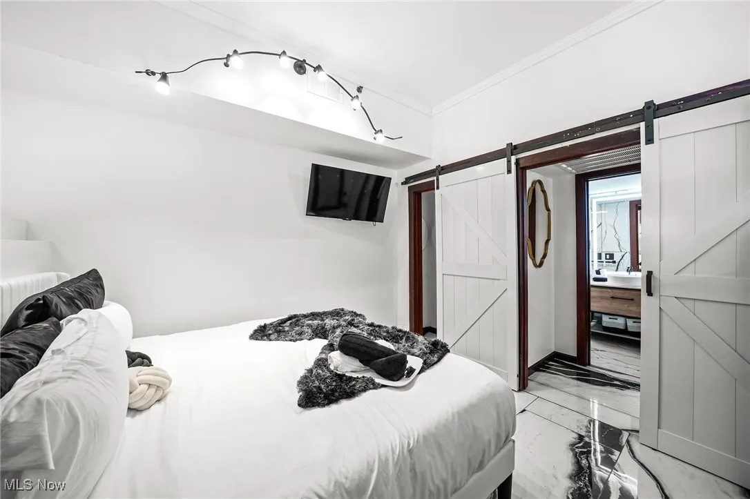 Bedroom featuring a barn door, light marble finish flooring, and crown molding