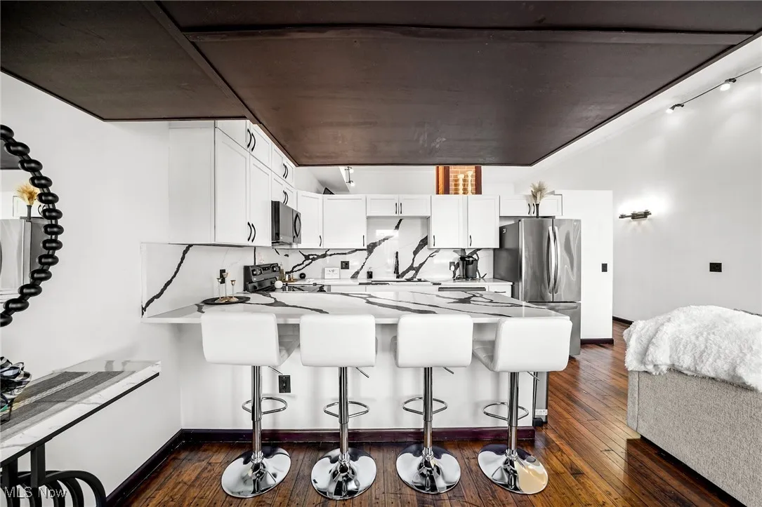 Kitchen featuring a peninsula, a kitchen bar, appliances with stainless steel finishes, light countertops, and white cabinets