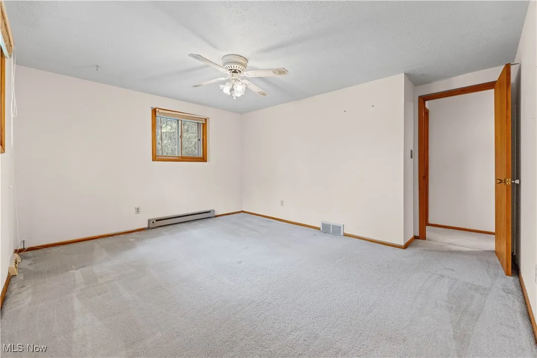 Spare room featuring a ceiling fan, carpet flooring, and a baseboard heating unit