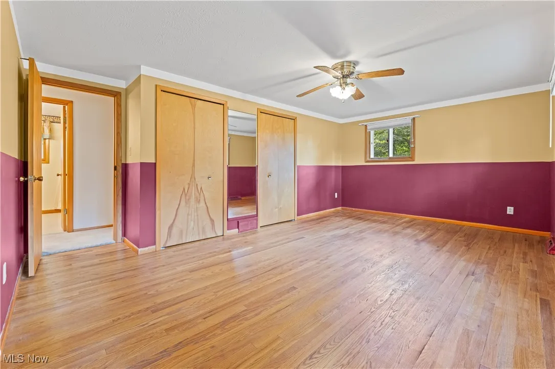 Primary bedroom with wood finished floors, dual closets, a ceiling fan, and crown molding