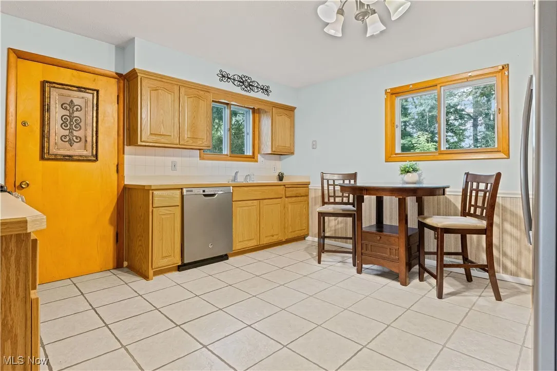 Eat-in kitchen featuring stainless appliances, light countertops, dishwasher, light tile floors, and tasteful backsplash. Entrance to the garage is through the door.