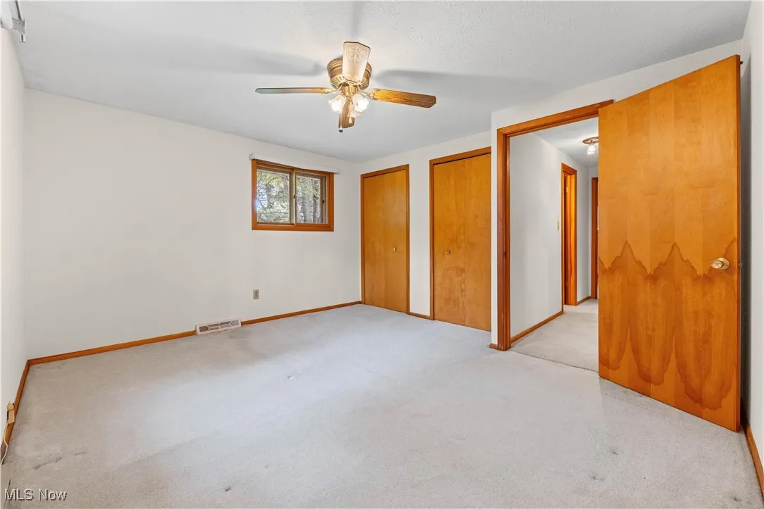 Bedroom with two closets, light colored carpet, and ceiling fan