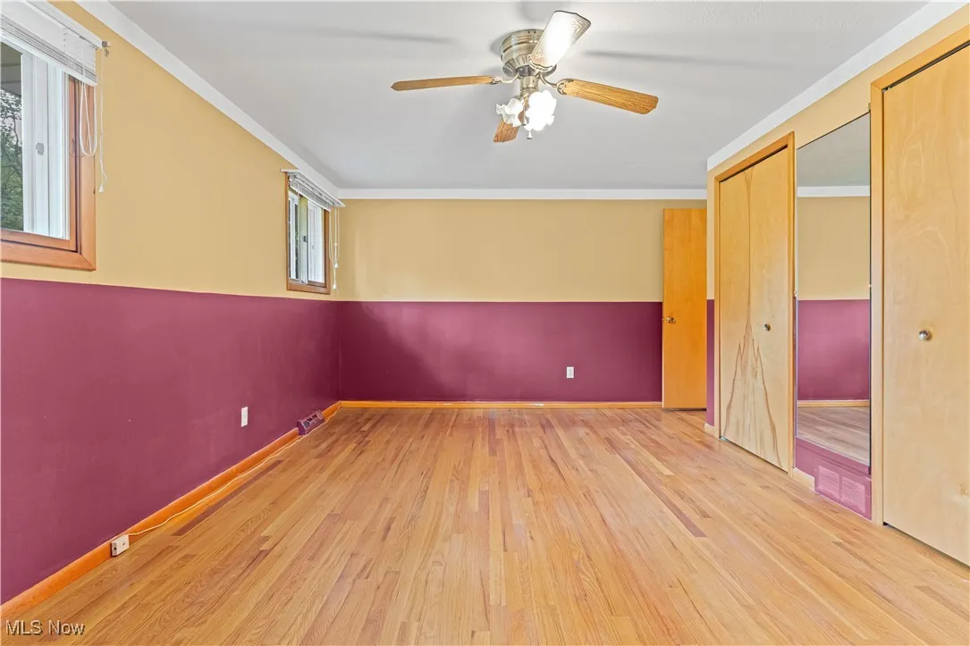Primary bedroom featuring dual closets, wood flooring, ornamental molding, and ceiling fan