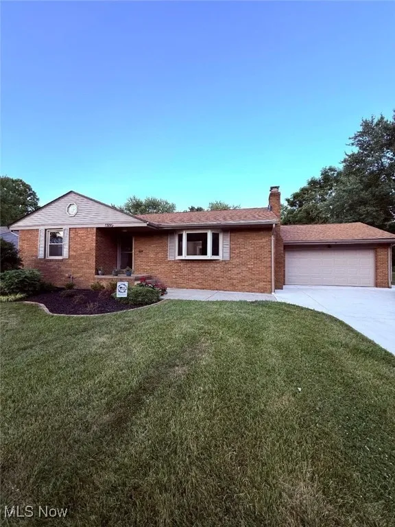Ranch-style home featuring an attached garage, driveway, a front yard, a chimney, and brick siding