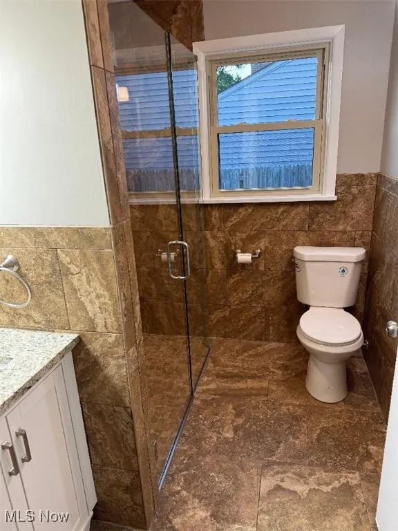Bathroom with tile walls, vanity, a stall shower, and a wainscoted wall