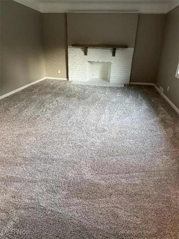 Empty room featuring carpet and a brick fireplace