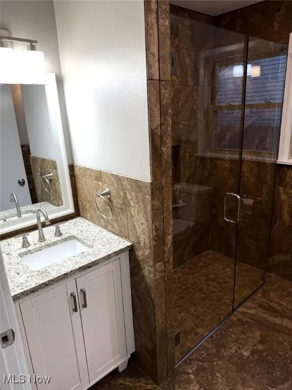 Full bath featuring a shower stall, vanity, tile walls, and wainscoting