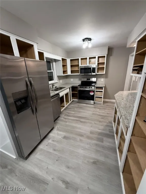 Kitchen with open shelves, appliances with stainless steel finishes, light stone counters, and light wood-type flooring