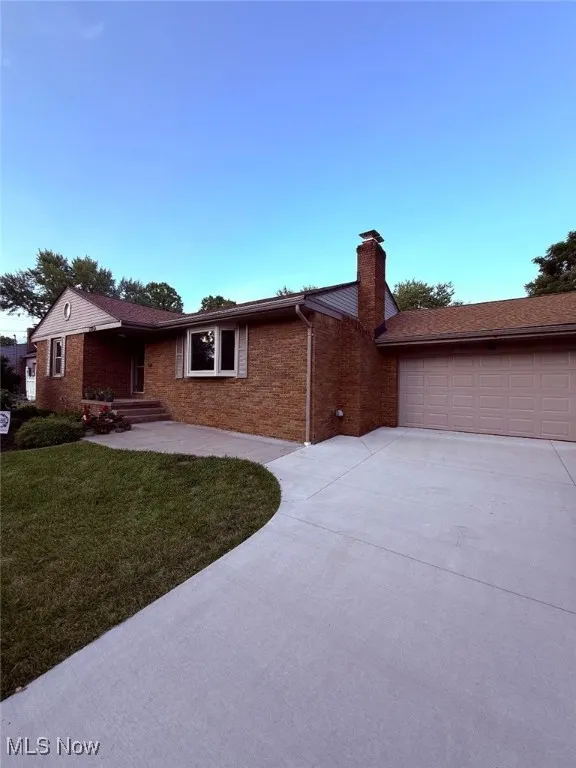 Ranch-style home with a garage, driveway, a front yard, a chimney, and brick siding