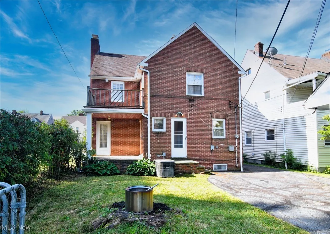Rear view of house featuring a balcony, brick siding, a chimney, and a yard