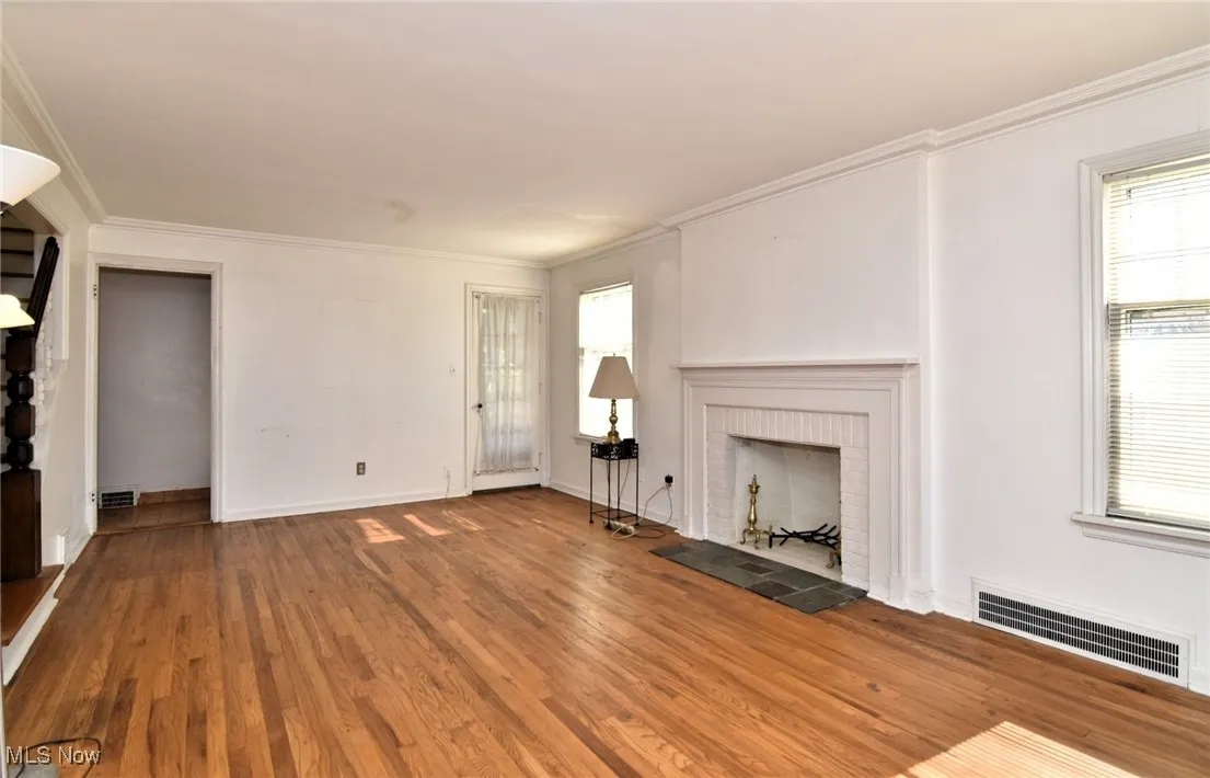  living room featuring a brick fireplace, wood finished floors, and crown molding