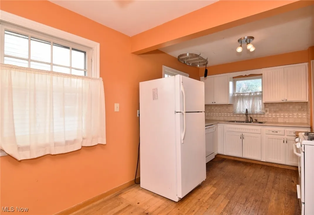 Kitchen with white appliances, light wood-style floors, backsplash, white cabinets, and light countertops