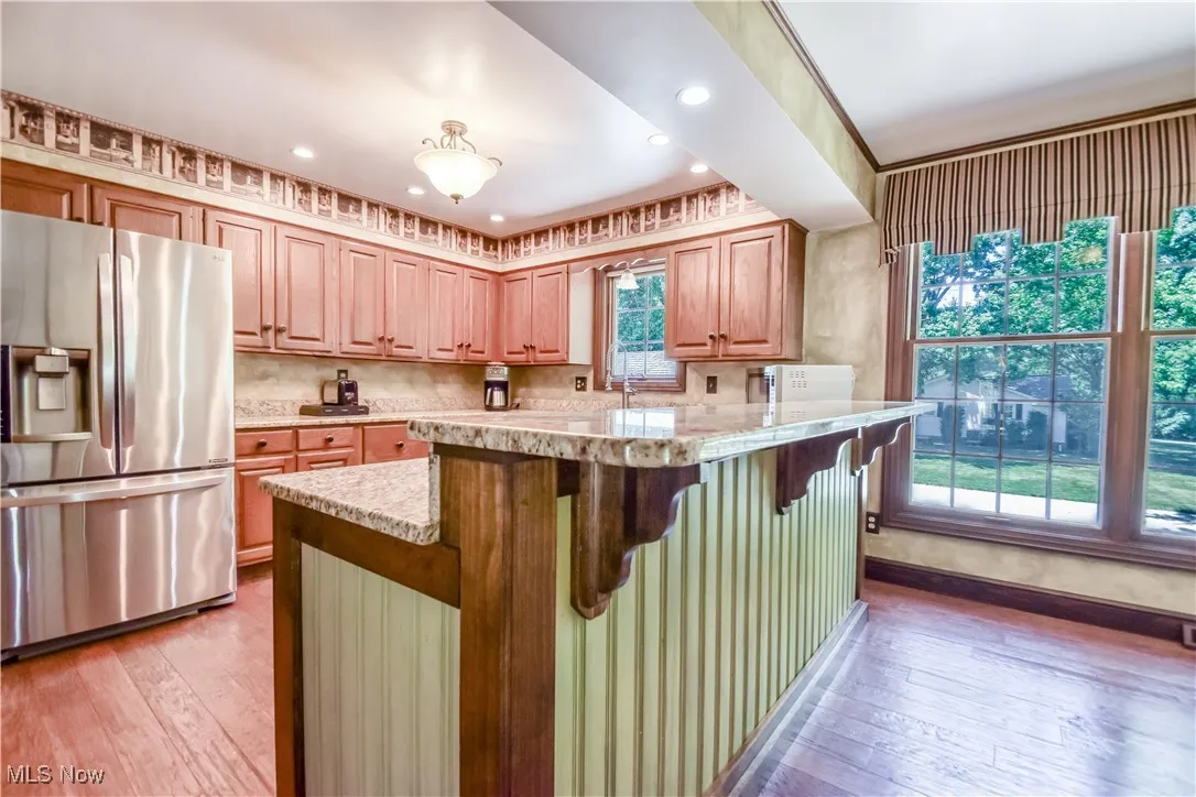 Kitchen featuring stainless steel fridge with ice dispenser, light wood-style flooring, a kitchen breakfast bar, recessed lighting, and tasteful backsplash