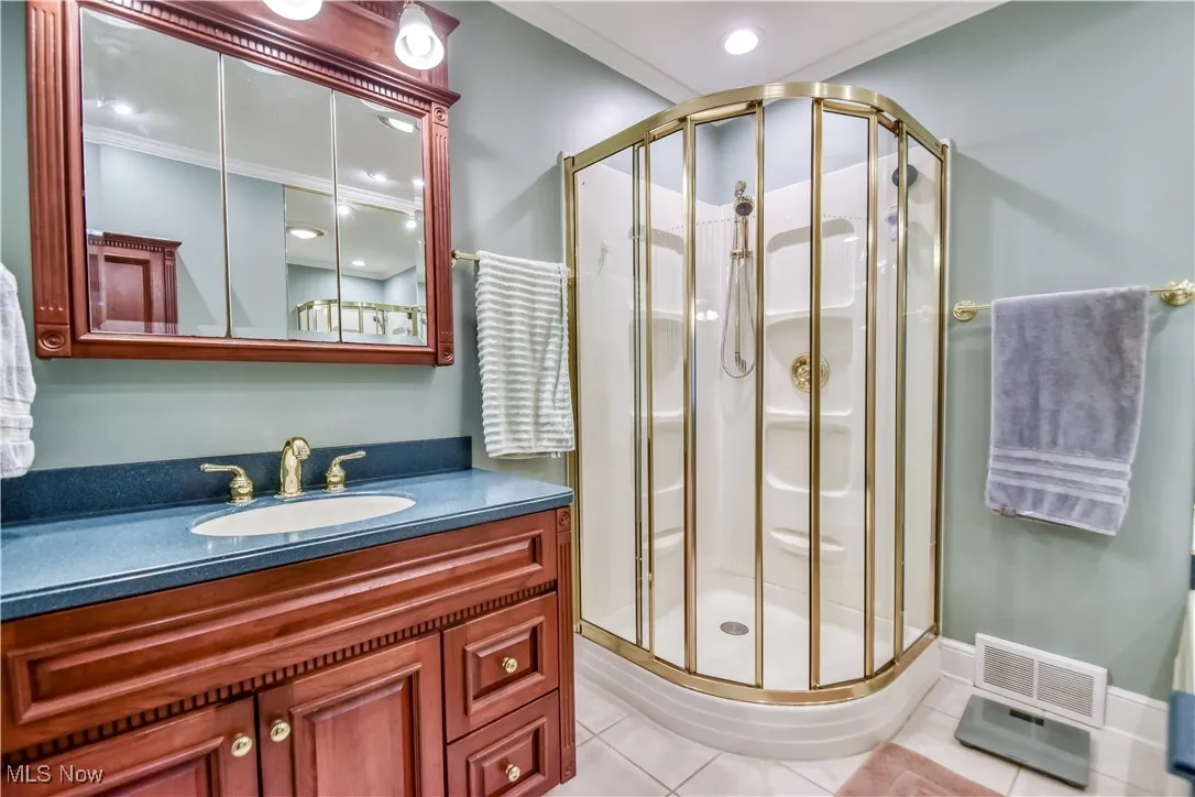 Full bathroom featuring a stall shower, vanity, tile patterned flooring, and crown molding