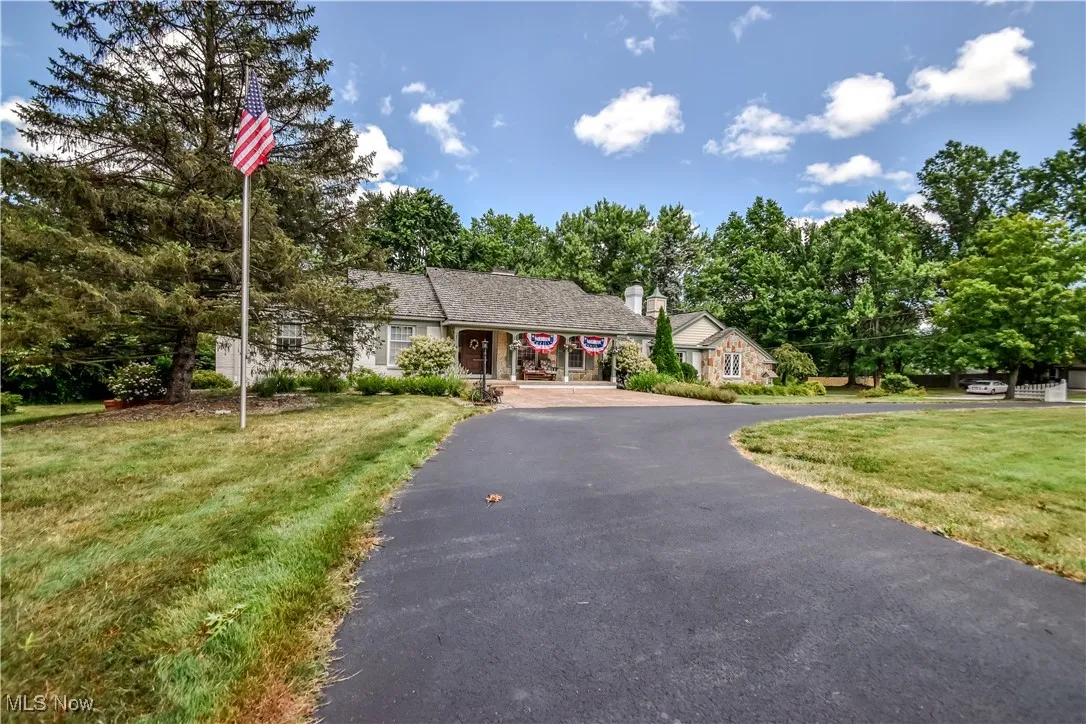View of front of house featuring driveway, a front lawn, a chimney, and view of scattered trees