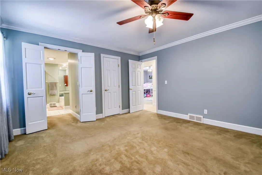 Unfurnished bedroom with ornamental molding, carpet flooring, ensuite bathroom, and ceiling fan