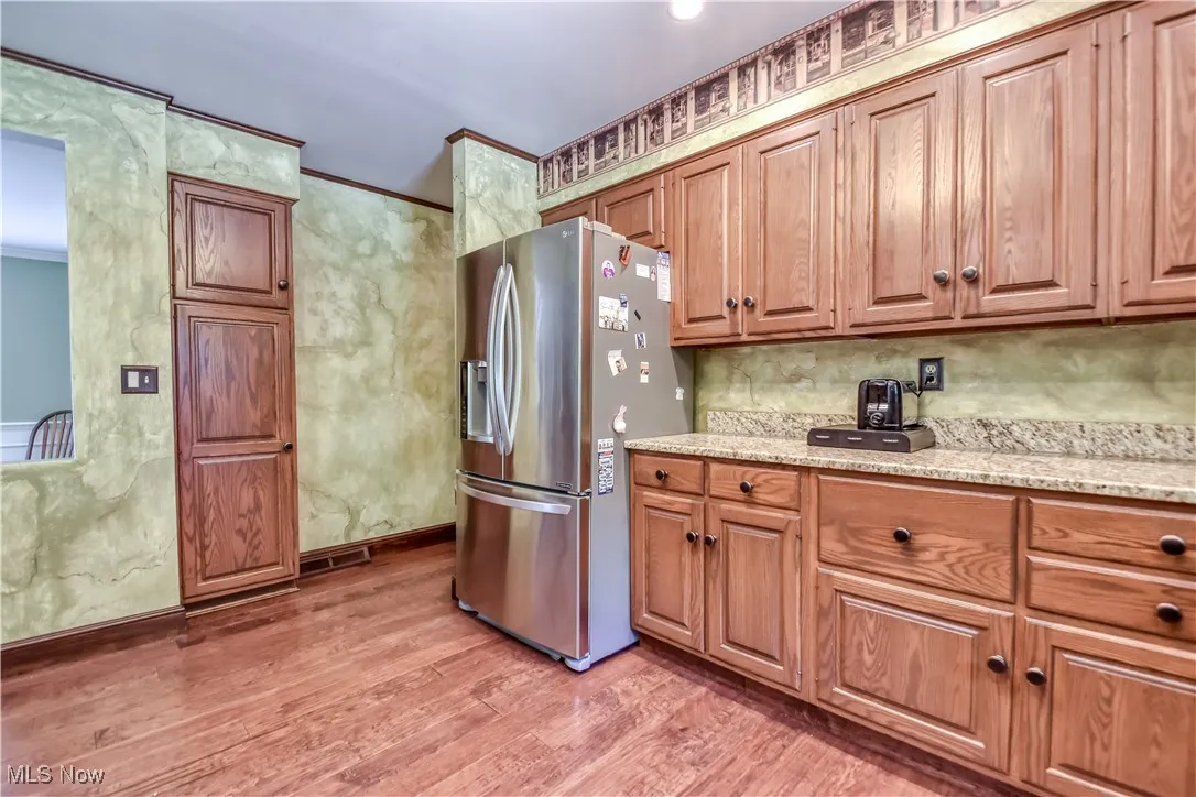 Kitchen featuring stainless steel fridge with ice dispenser, light wood-type flooring, brown cabinetry, light stone counters, and decorative backsplash