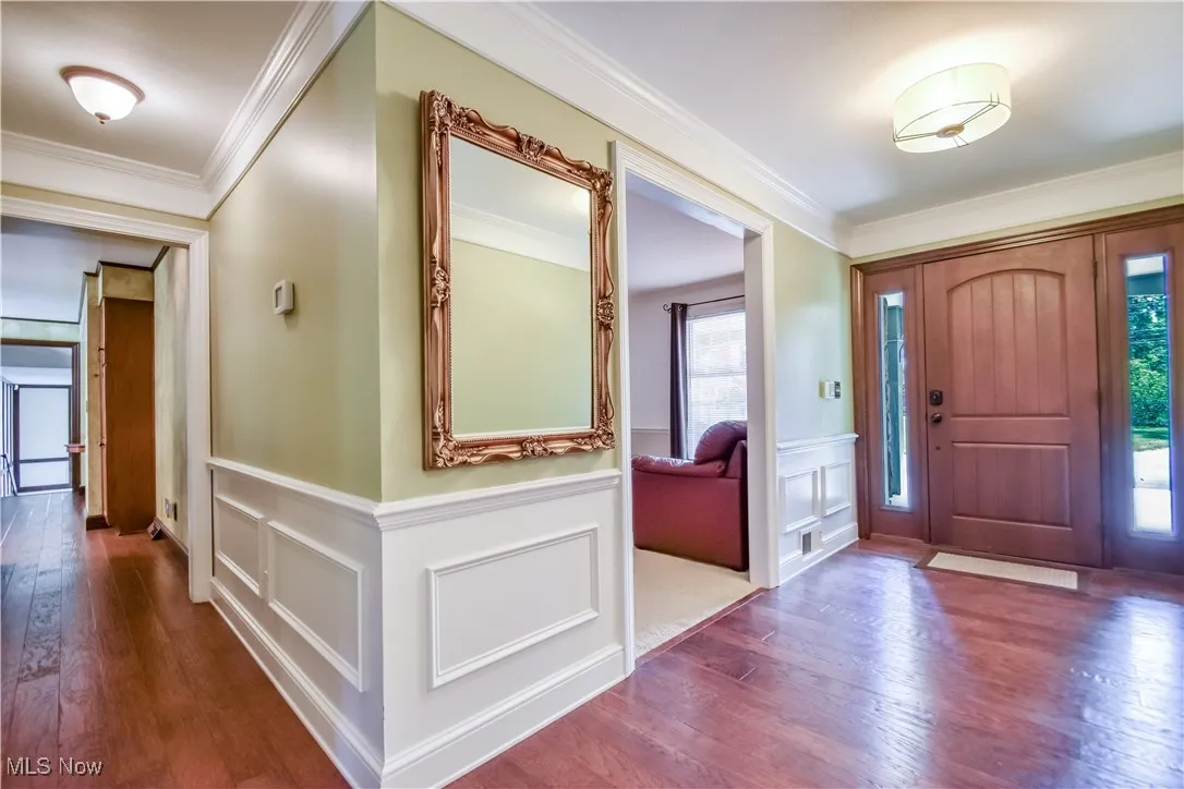 Foyer featuring plenty of natural light, wood finished floors, ornamental molding, wainscoting, and a decorative wall