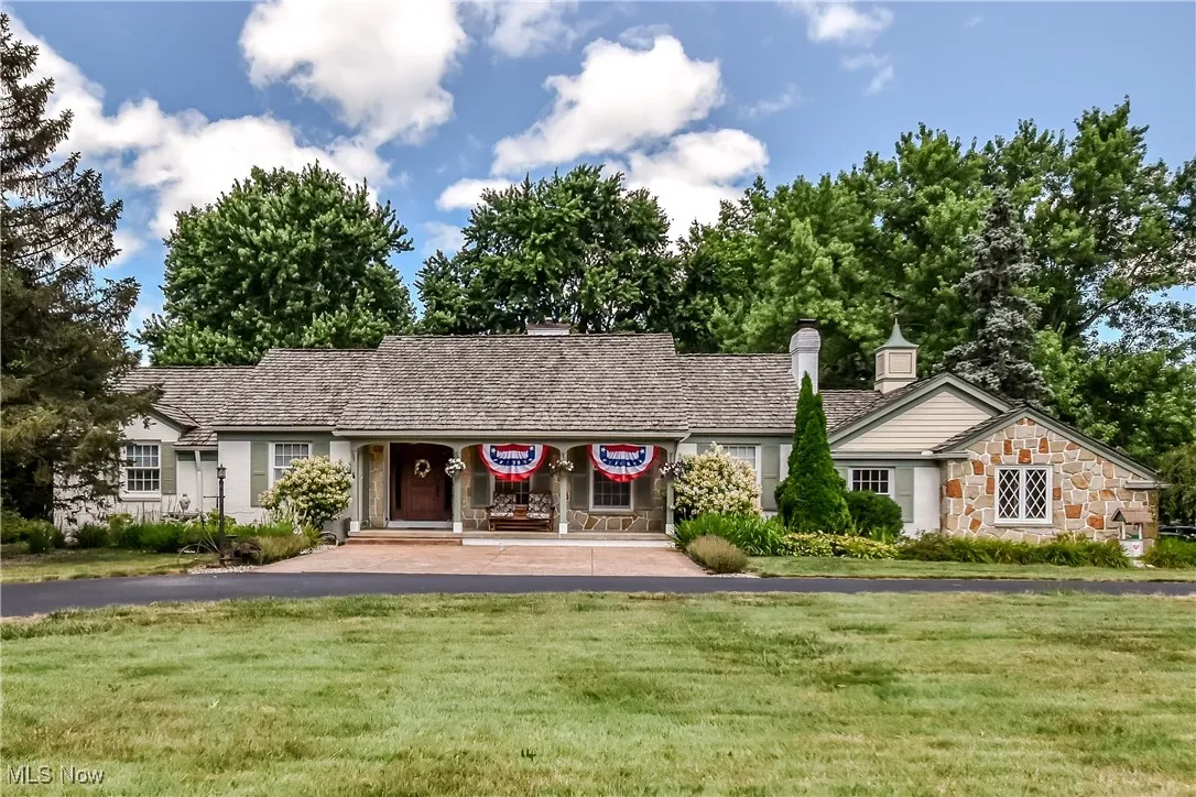 Ranch-style house featuring a front lawn, a chimney, and stone siding