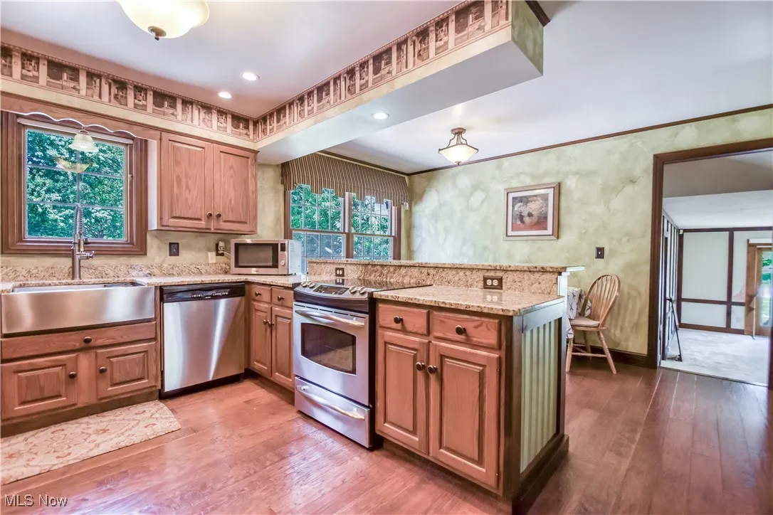 Kitchen with stainless steel appliances, a peninsula, wood finished floors, and light stone countertops