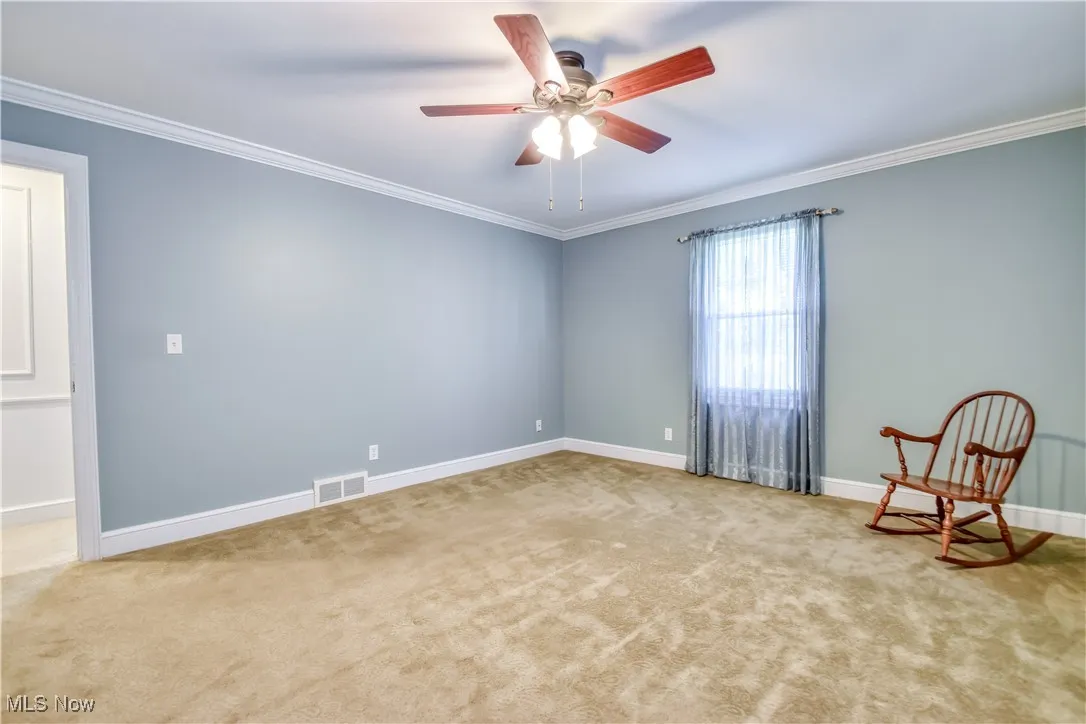 Carpeted empty room featuring crown molding and a ceiling fan
