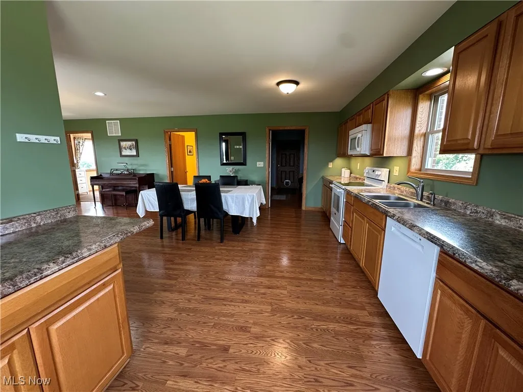 Kitchen with healthy amount of natural light, white appliances, dark countertops, dark wood-type flooring, and recessed lighting