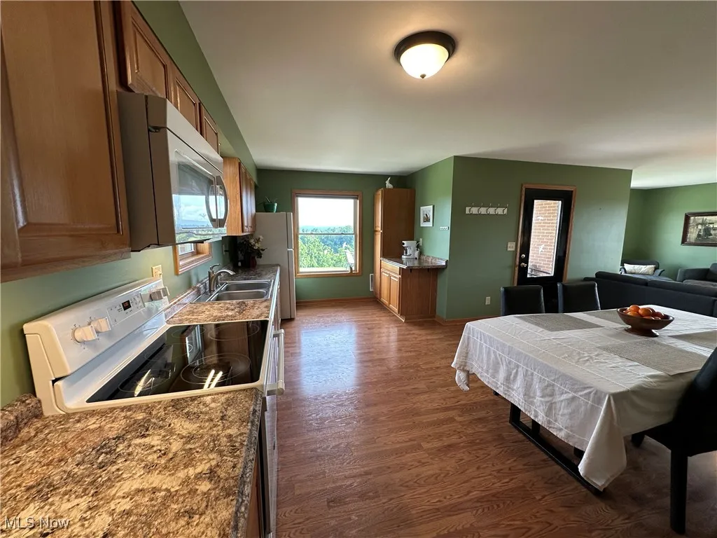 Kitchen featuring white appliances, dark wood-style floors, brown cabinetry, and open floor plan