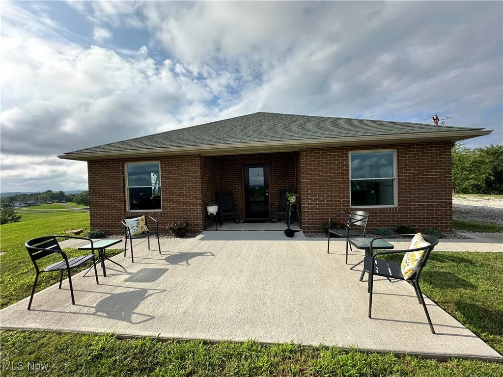 Rear view of property featuring roof with shingles, brick siding, a patio area, and a lawn