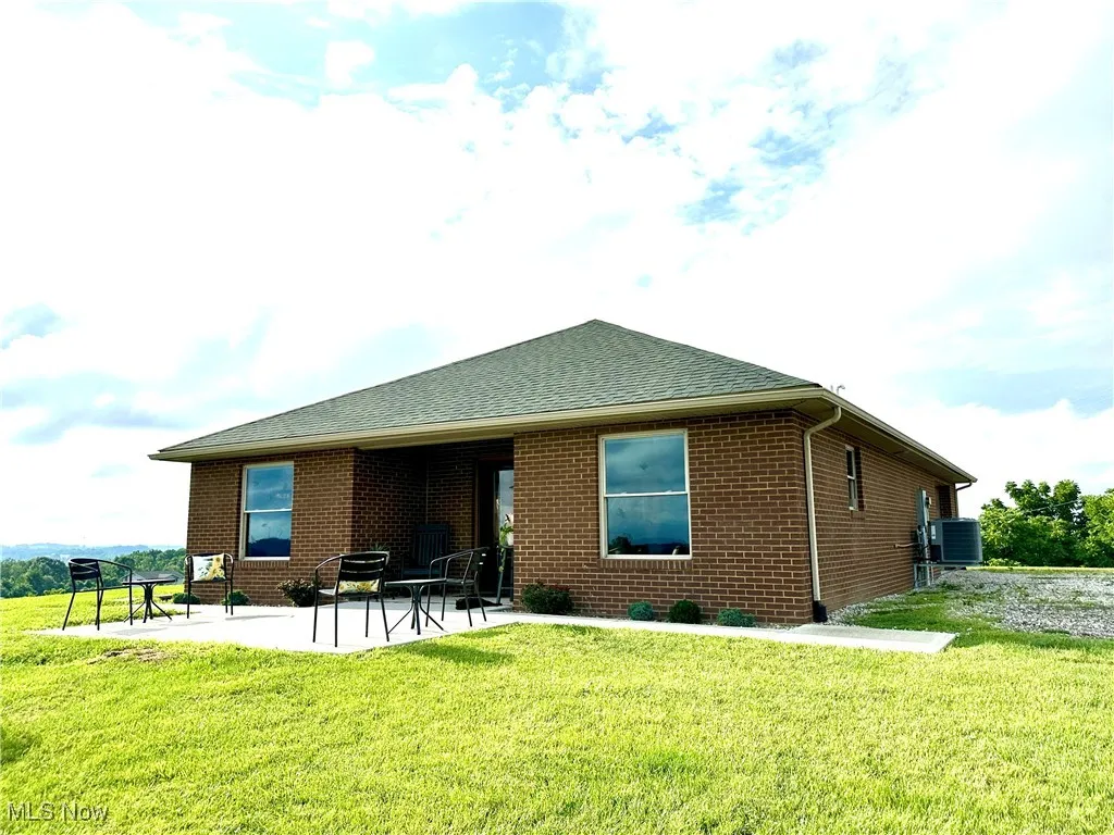 Back of house featuring brick siding, a shingled roof, a lawn, and a patio area