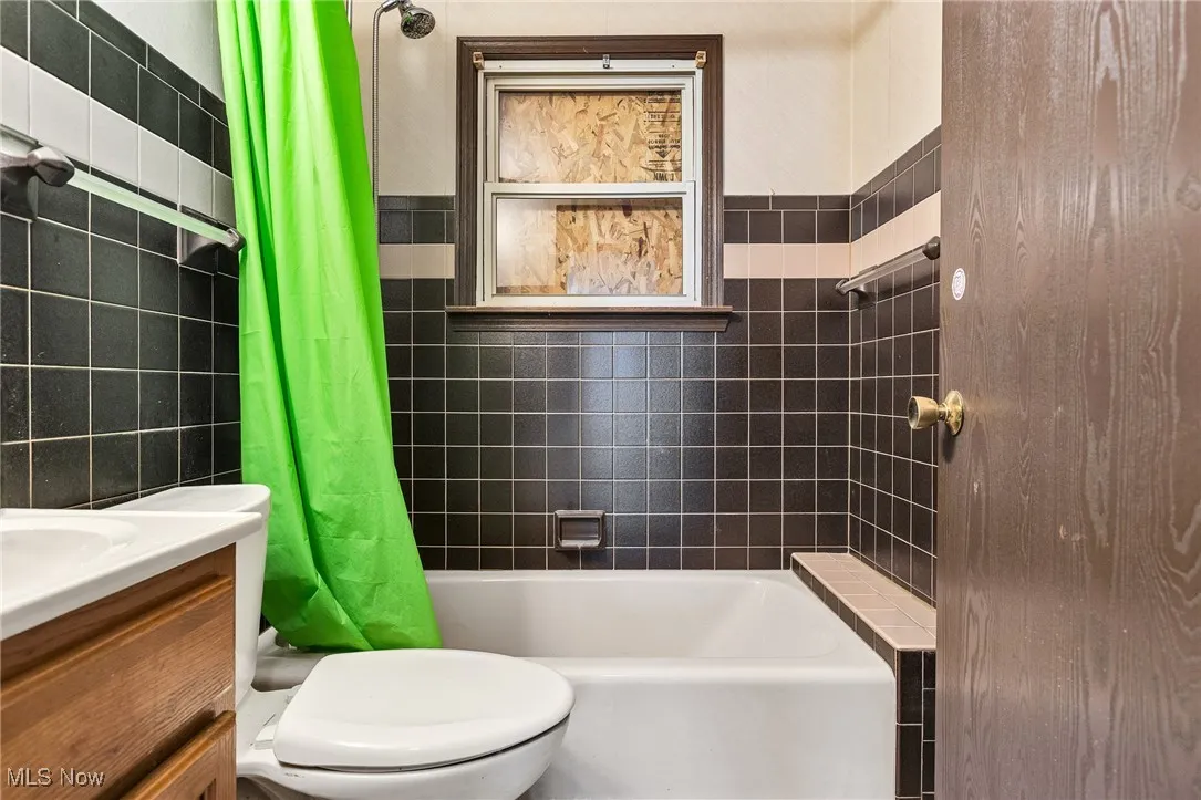 Bathroom featuring tile walls, shower / tub combo with curtain, and vanity