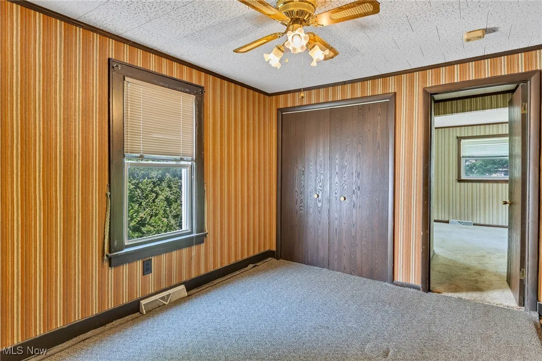 Unfurnished bedroom featuring carpet flooring, ornamental molding, a closet, and a ceiling fan