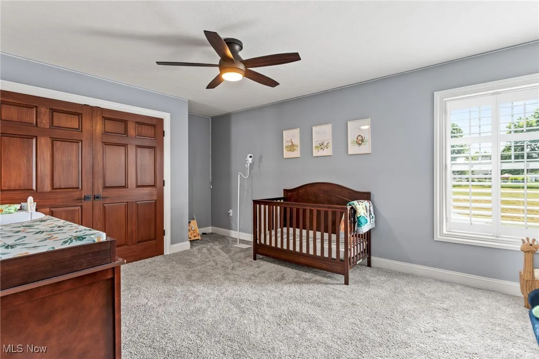 Bedroom with light colored carpet, a nursery area, a ceiling fan, and a closet