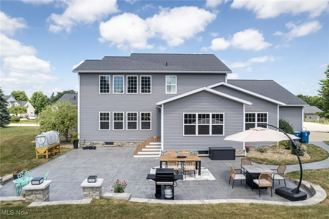 Rear view of house featuring a patio, roof with shingles, and a lawn